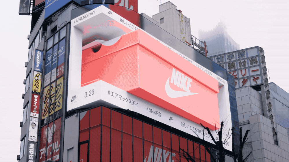 Animated GIF of a 3D Nike shoes ad on a large outdoor LED building display by Visual Lab, delivering immersive visuals and high-impact digital signage for advertising.صورة GIF متحركة لإعلان ثلاثي الأبعاد لأحذية Nike على شاشة إل إي دي خارجية كبيرة على مبنى من فيجوال لاب، تقدم تجربة عرض غامرة وإعلانات رقمية عالية التأثير.
