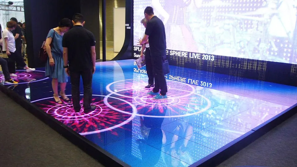Group of people interacting with a floor LED display by standing on it, demonstrating Visual Lab’s immersive interactive walkable screen technology for events and exhibitions.مجموعة أشخاص يقفون على شاشة إل إي دي أرضية تفاعلية من فيجوال لاب، تعرض تجربة عرض رقمية غامرة وقابلة للمشي في فعالية.