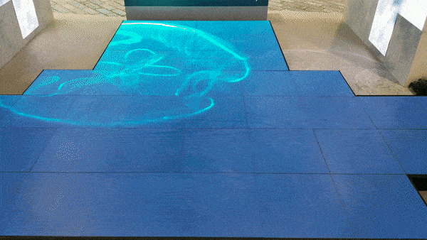 Animated GIF showcasing a floor LED display by Visual Lab with flowing wave animations across the surface, highlighting immersive interactive display technology.صورة GIF متحركة لشاشة إل إي دي أرضية من فيجوال لاب تعرض تأثيرات أمواج متحركة على السطح، لتوضيح تقنية الشاشات التفاعلية الغامرة.
