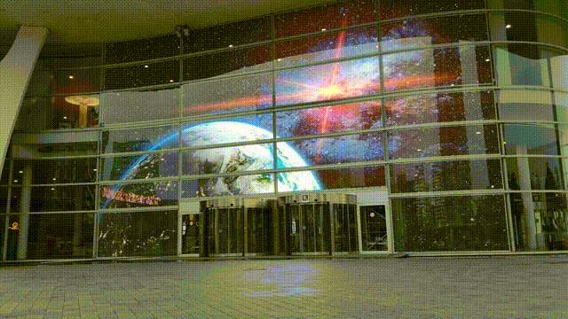 Animated GIF of a transparent LED display by Visual Lab showcasing space and planets, demonstrating immersive see-through digital display technology.صورة GIF متحركة لشاشة إل إي دي شفافة من فيجوال لاب تعرض الفضاء والكواكب لتوضيح تقنية العرض الشفافة الغامرة.